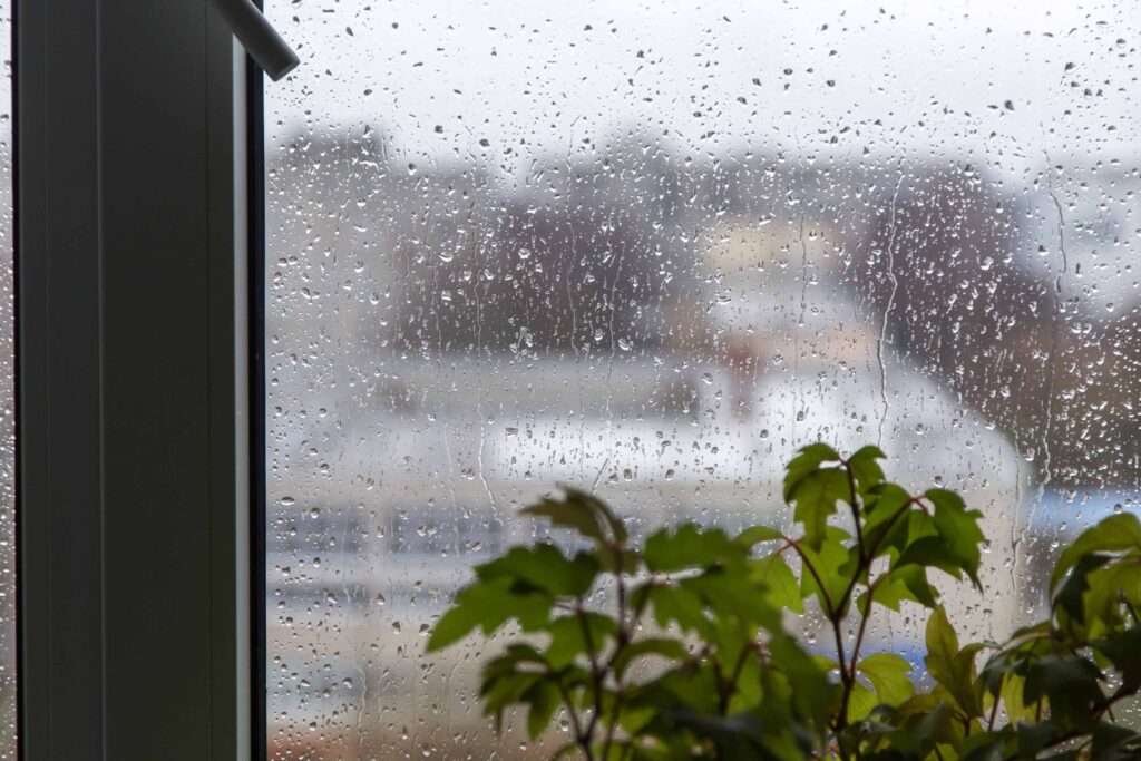 Rain drops on window glass close up background texture. View on rainy street, town from home