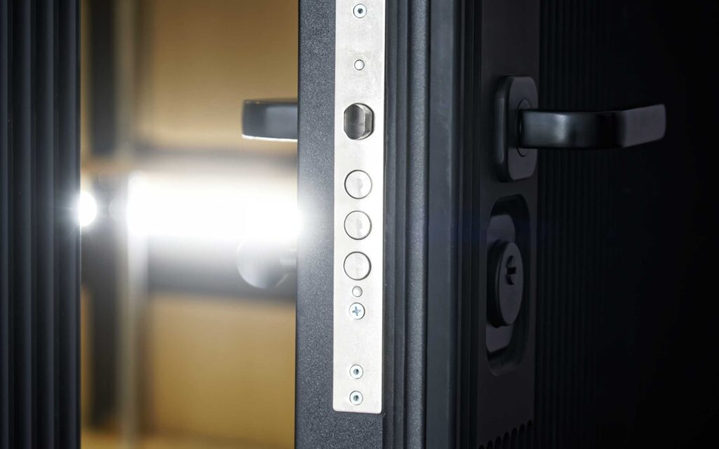 Close-up of a modern metallic door lock mechanism with dual black handles and a visible keyhole, illuminated by light through the door gap.