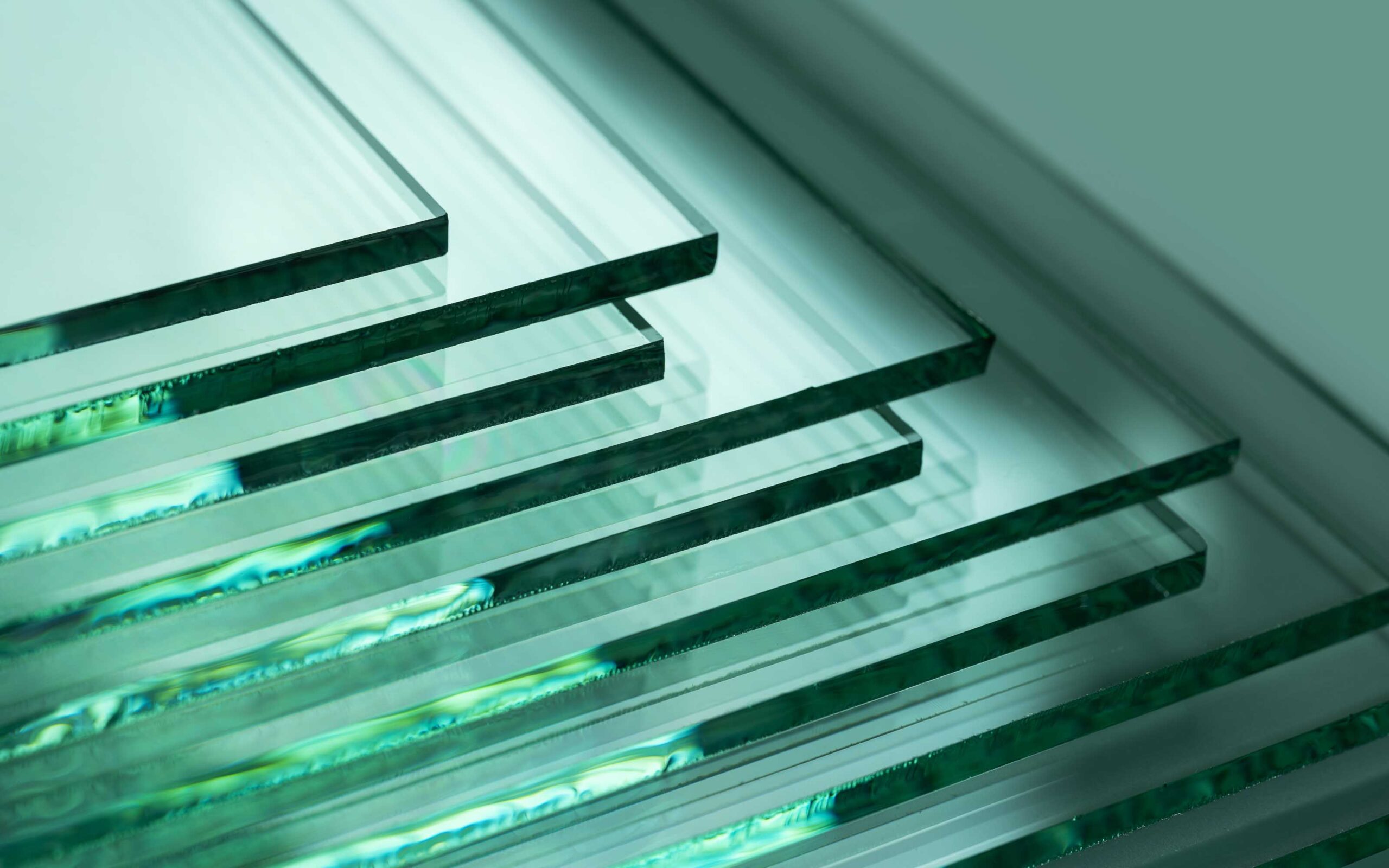Stack of clear rectangular glass sheets with green-tinted edges, fanned out to highlight their transparency and reflective surfaces.